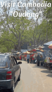 a car is parked on the side of the road in front of a market called oudong in cambodia