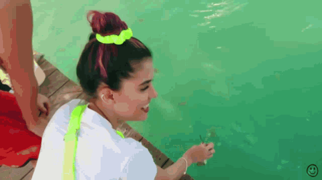 a woman in a neon green scrunchie is looking at a fish in the water