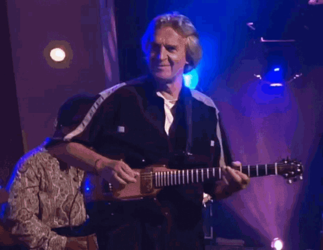 a man playing a guitar in a dark room with blue lights behind him