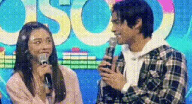 a man and a woman are standing next to each other on a stage holding microphones .