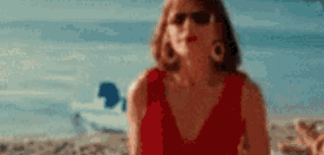 a woman wearing sunglasses and a red dress is standing on a beach .