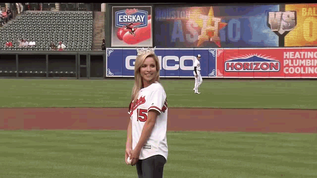 a woman stands on a baseball field in front of a gico ad