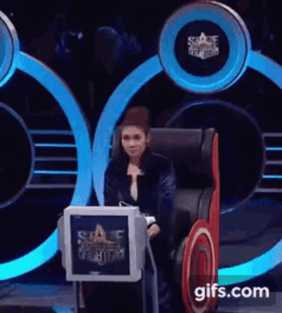 a woman is sitting in a chair in front of a podium that says ' sonic the hedgehog ' on it .
