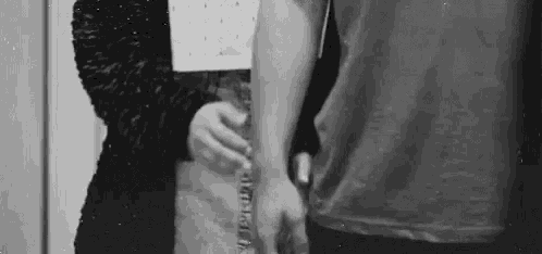 a man and a woman are holding hands in a black and white photo . the woman is measuring the man 's arm .