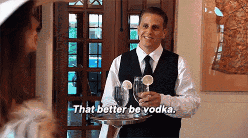 a man in a vest and tie is holding a tray with glasses on it and says that better be vodka