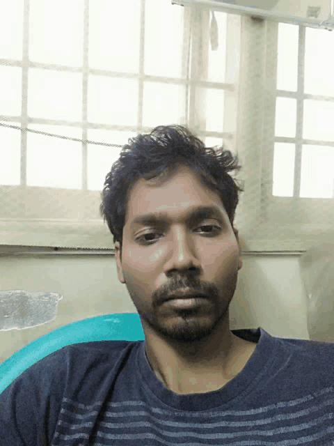 a man with a beard is sitting in front of a window and looking at the camera