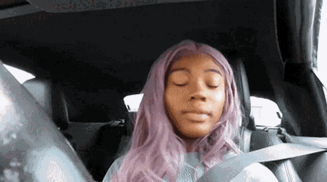 a woman with purple hair sits in the back seat of a car with her eyes closed