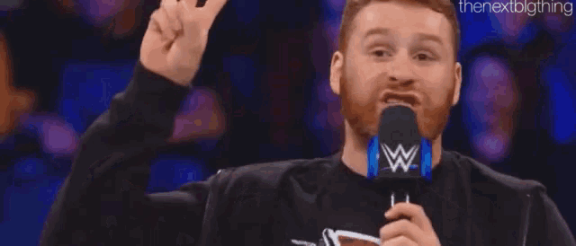 a man with a beard is giving a peace sign while holding a microphone .