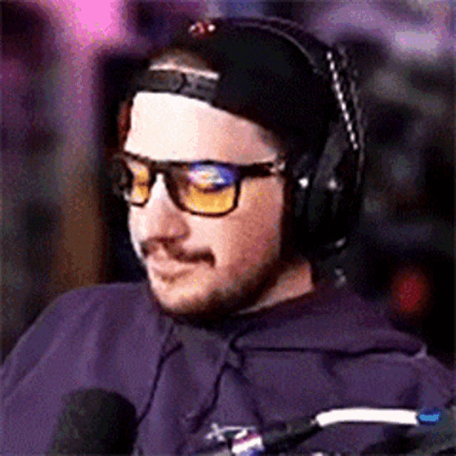 a man wearing headphones and glasses sitting in front of a microphone .
