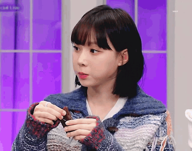 a girl in a sweater is holding a piece of chocolate in her hands