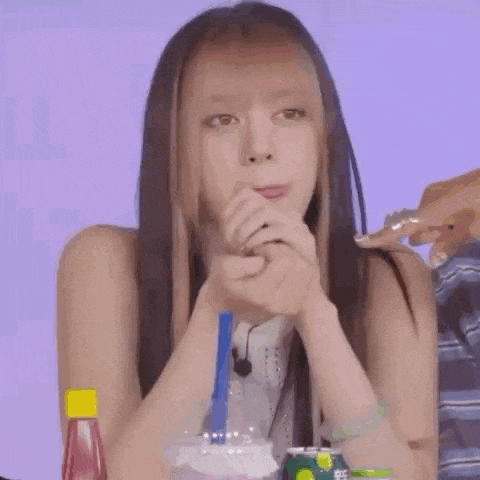 a woman with long hair is sitting at a table with a drink in her hand and looking at the camera .