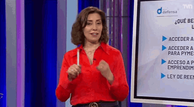 a woman in a red shirt is standing in front of a tv screen .