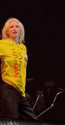 a woman wearing a yellow shirt that says ' usn ' on it is singing into a microphone