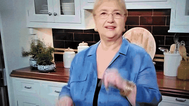 a woman in a blue shirt and glasses is standing in a kitchen