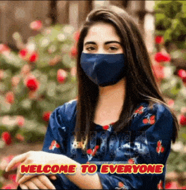 a woman wearing a blue face mask is standing in front of flowers with the words welcome to everyone below her