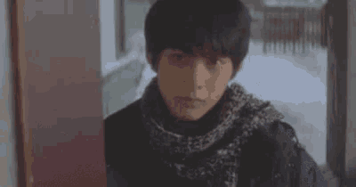 a young man in a scarf is standing in front of a door .