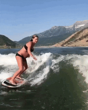 a pregnant woman in a bikini is riding a wave on a surfboard