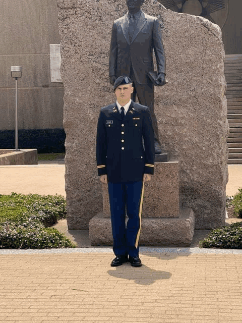a man in a military uniform stands in front of a statue of a man