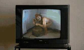 a tv screen shows a man squatting down with a box in his hand