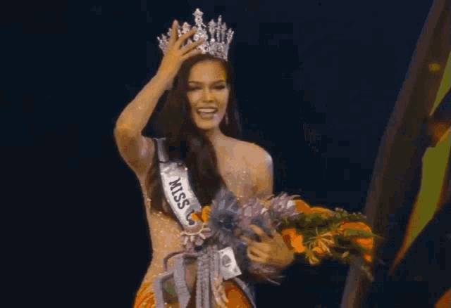a woman is holding a bouquet of flowers and wearing a crown and miss universe sash .