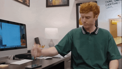 a man in a green shirt is sitting at a desk