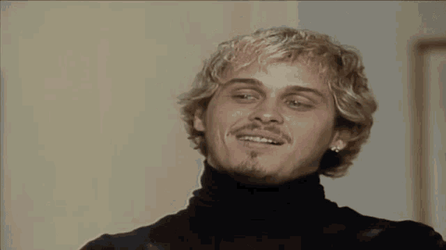 a man with blonde hair and a beard wearing a black turtleneck sweater