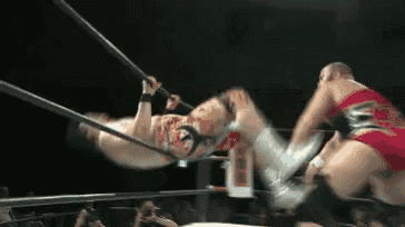 two wrestlers are wrestling in a ring with a crowd in the stands watching .