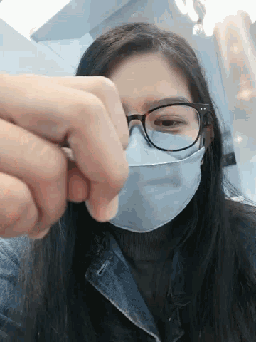a woman wearing glasses and a face mask holds her hand over her face