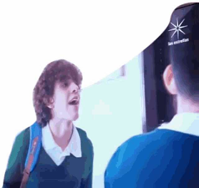 a boy in a green sweater is talking to another boy in a blue shirt that says las estrellas