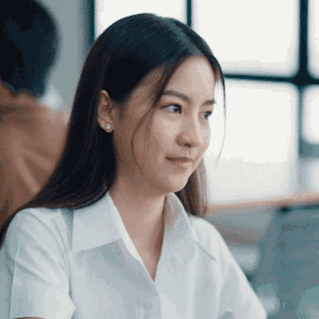 a woman wearing a white shirt and earrings smiles