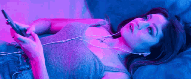 a woman is listening to music on her phone while laying on a bed