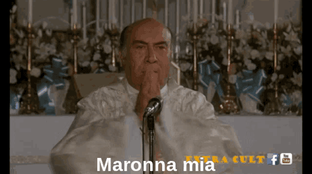 a man praying in front of a microphone with the words maronna mia on the bottom of the screen