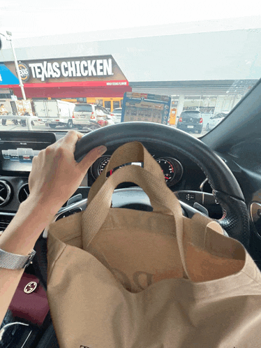 a person driving a car with a bag in front of a texas chicken restaurant