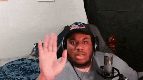 a man wearing headphones and a hat is waving at the camera .
