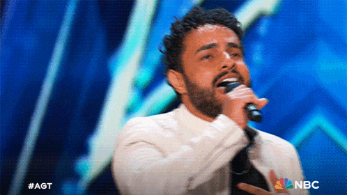 a man singing into a microphone with a nbc logo in the background