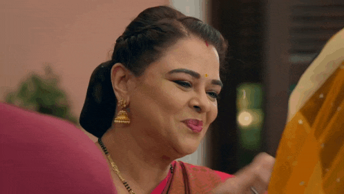 a woman wearing a red sari and gold earrings smiles