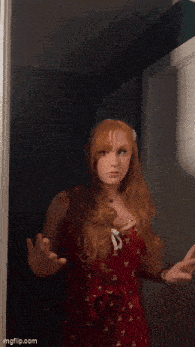 a woman with red hair is standing in front of a door with her hands outstretched