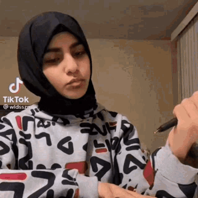 a woman in a hijab is holding a pen and writing on her hand .