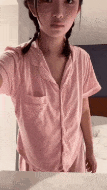 a woman in a pink pajama shirt is taking a selfie in front of a mirror .