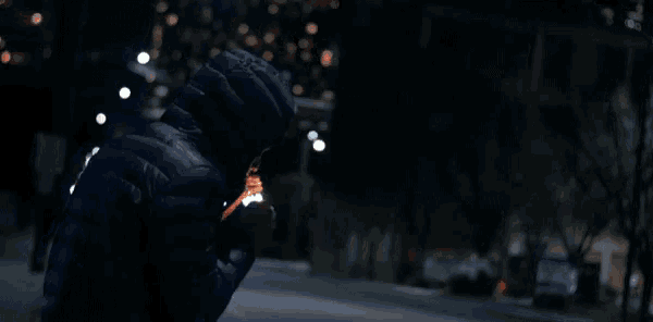 a person in a hooded jacket is looking at their phone in the dark