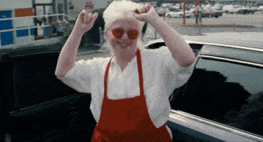a woman wearing a red apron and red sunglasses is standing in front of a car