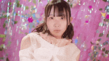 a young girl is standing in front of a pink background and blowing a kiss .