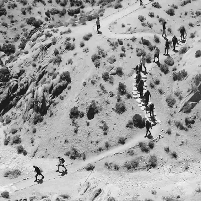 a black and white photo of a group of people hiking up a mountain