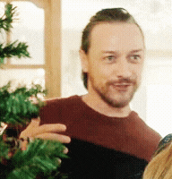 a man with a beard is standing in front of a christmas tree .
