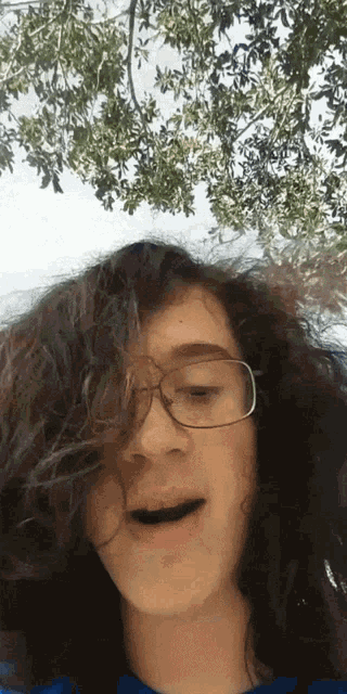 a girl with curly hair wearing glasses looks at the camera