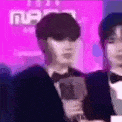 a man in a tuxedo is holding a microphone in front of a pink background .