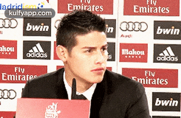 a man in a suit is sitting in front of a wall that says fly emirates on it