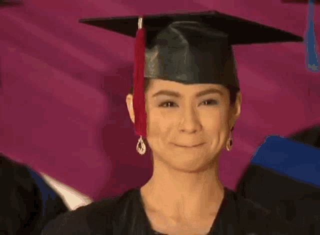 a woman wearing a graduation cap and gown is smiling and holding her hand in the air .