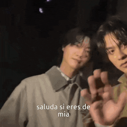 a couple of men standing next to each other with the words saluda si eres de mia written on the bottom .