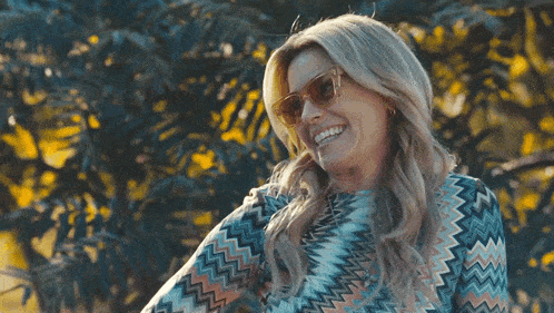 a woman wearing sunglasses and a patterned shirt smiles for the camera